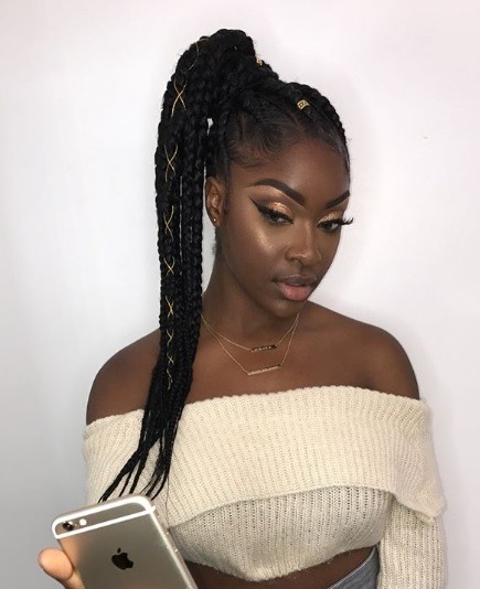 Coiffures d'hiver pour cheveux naturels : Photo d'une femme avec une longue queue de cheval brune avec des cheveux dorés, portant un pull de crème sur l'épaule et prenant un selfie sur son téléphone