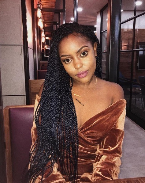 Coiffures d'hiver pour cheveux naturels : Photo d'une femme avec de longues torsades en forme de boîte marron foncé balayées sur une épaule, portant un velours marron sur la robe d'épaule