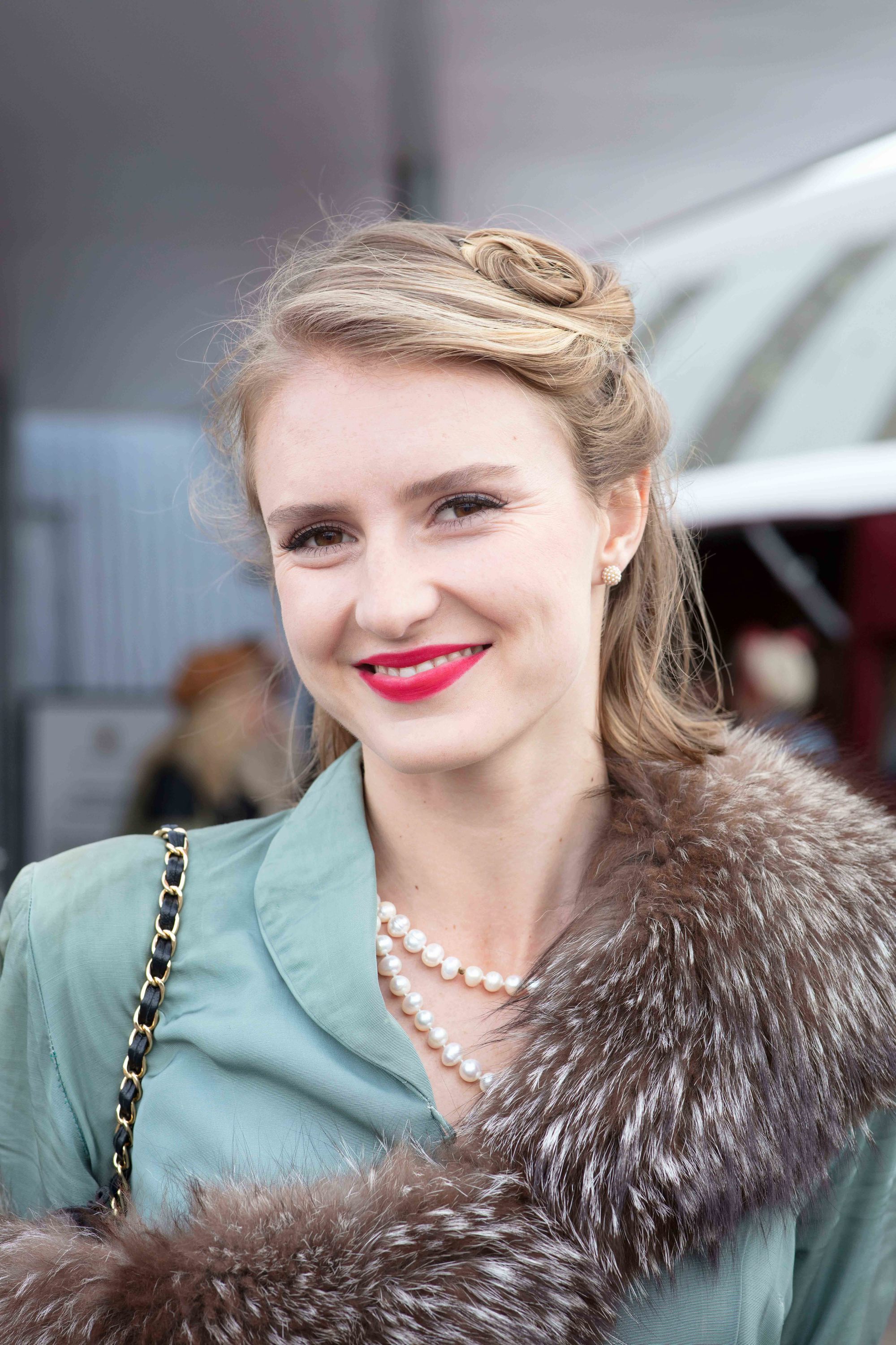 Cheveux courts vintage : Gros plan d'une femme aux cheveux courts, coiffée à moitié, à moitié duvet, avec une veste bleu canard, des perles et un jet au festival de Goodwood