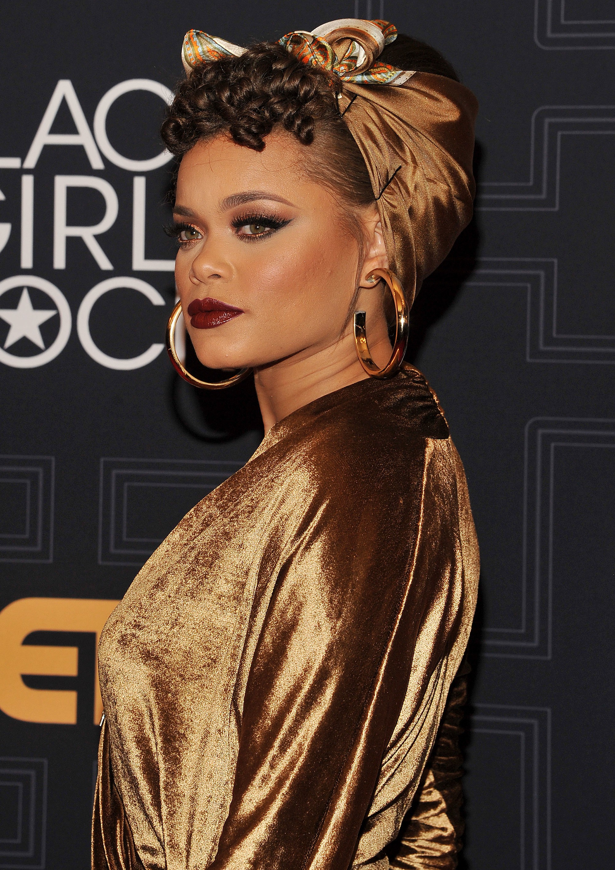 Cheveux courts vintage : Gros plan d'Andra Day avec ses cheveux courts enveloppés dans une écharpe, avec une fausse frange bouclée à l'avant sur le tapis rouge
