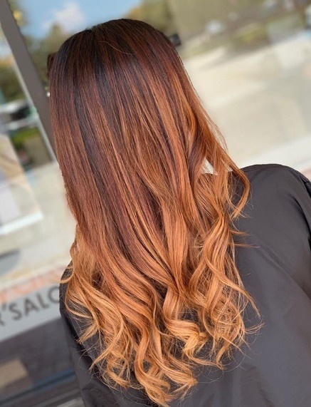 Femme avec de longs cheveux bouclés en cuivre de balayage