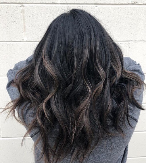 Femme aux cheveux noirs mi-longs et ondulés en balayage