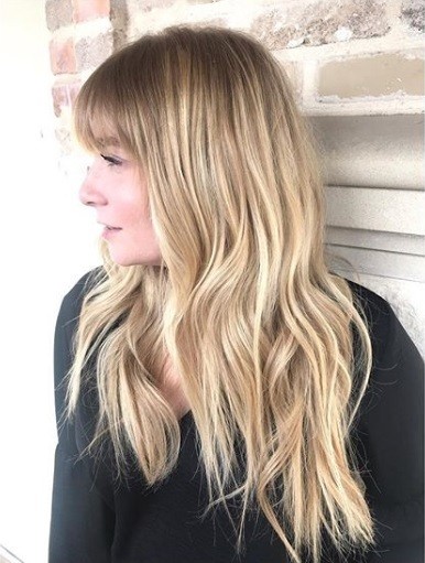 Femme aux longs cheveux blonds ondulés en balayage avec une frange