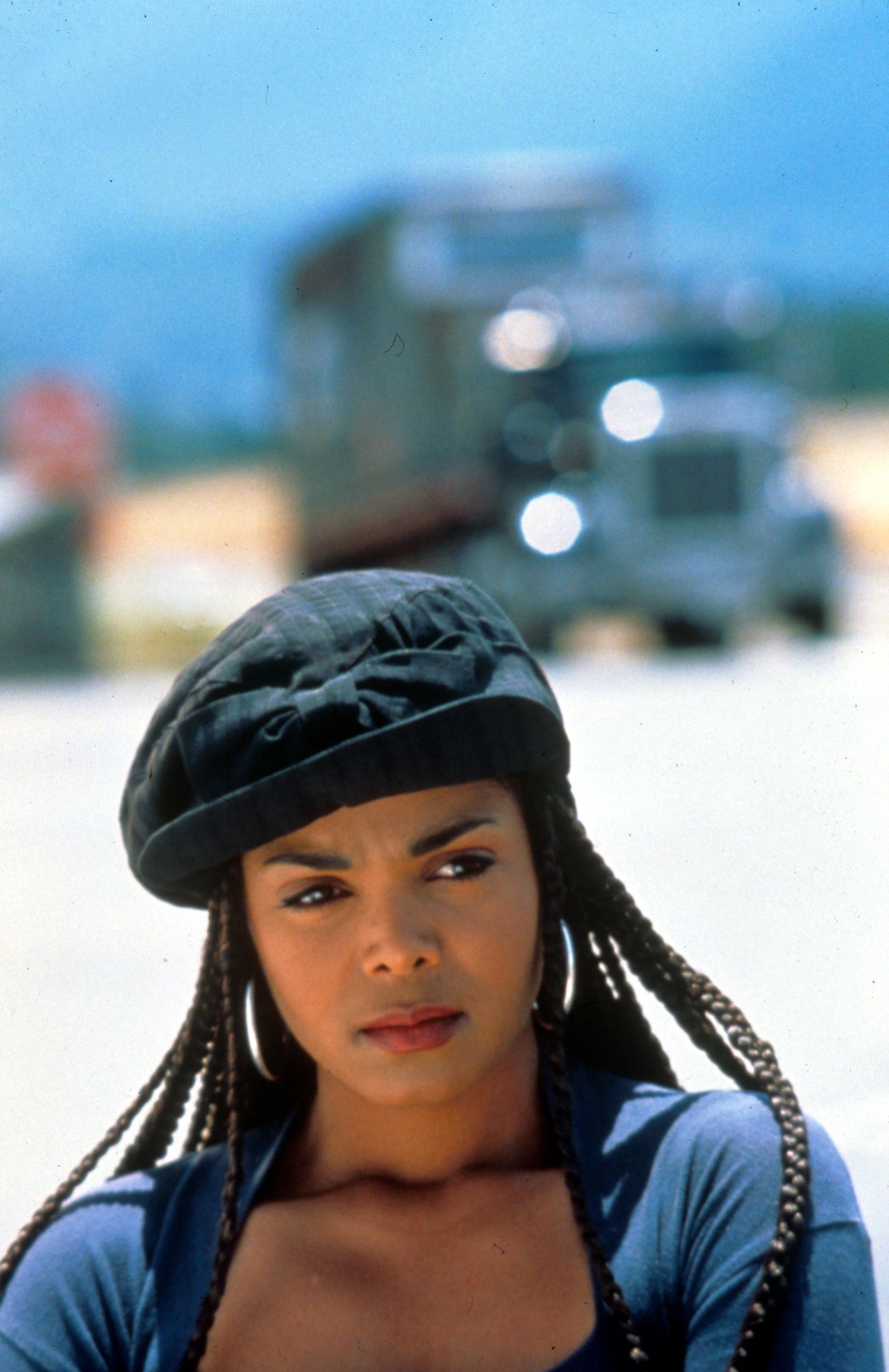 Coiffures des années 90 : Janet Jackson boxe des tresses du film Poetic Justice, portant un béret noir et des boucles d'oreilles en cerceau