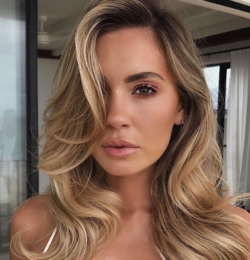 Femme avec de longs cheveux blonds coiffés en franges dramatiques, portant un bikini blanc et posant à l'extérieur.