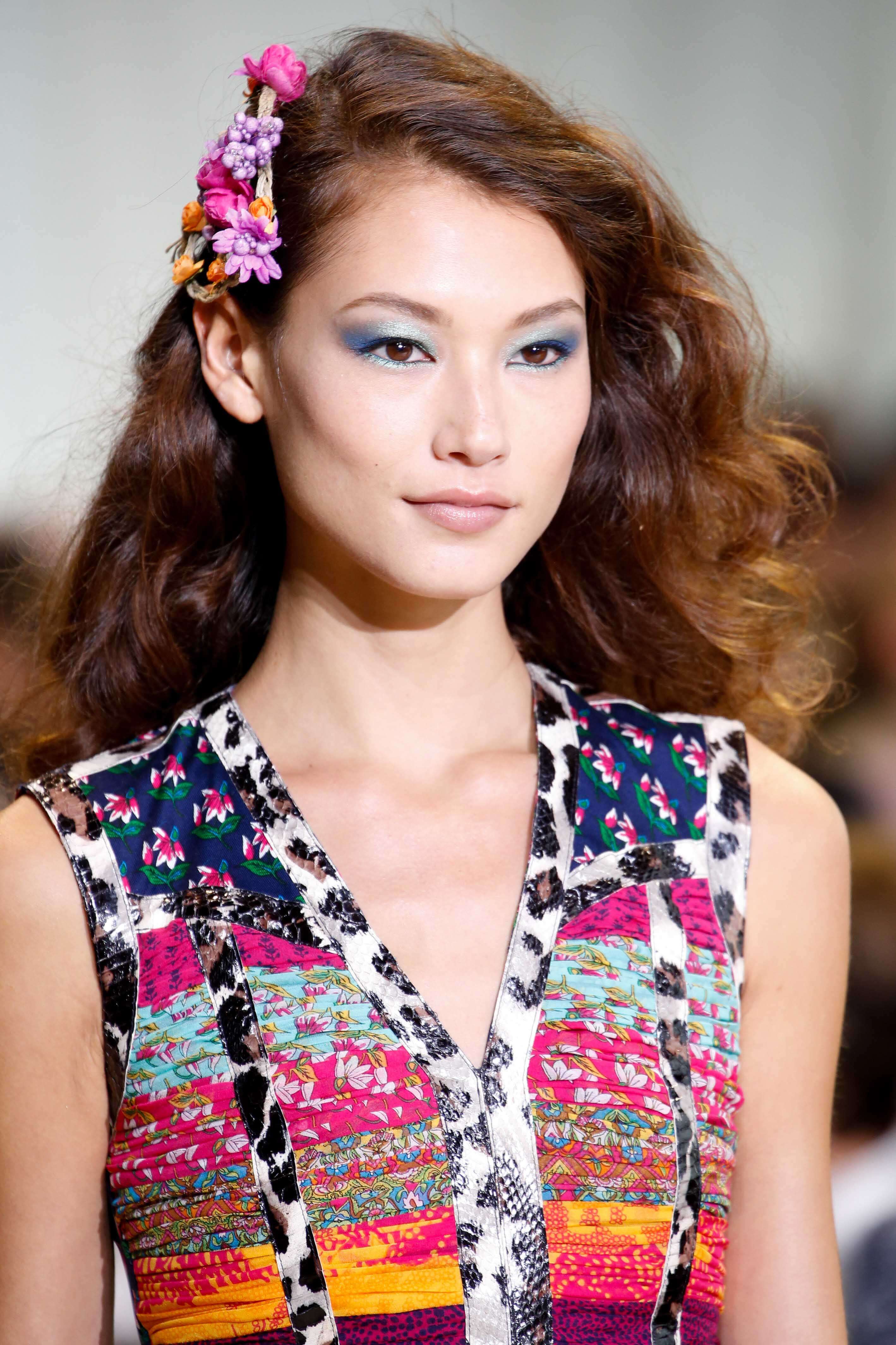 Coiffures asiatiques : Femme asiatique aux cheveux bouclés bruns caramels dorés avec un accessoire de cheveux floral portant une robe à motifs.