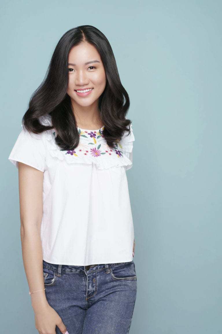 Coiffures asiatiques : Femme asiatique avec de longs cheveux bruns ondulés et bouclés, portant un haut blanc et un jean.