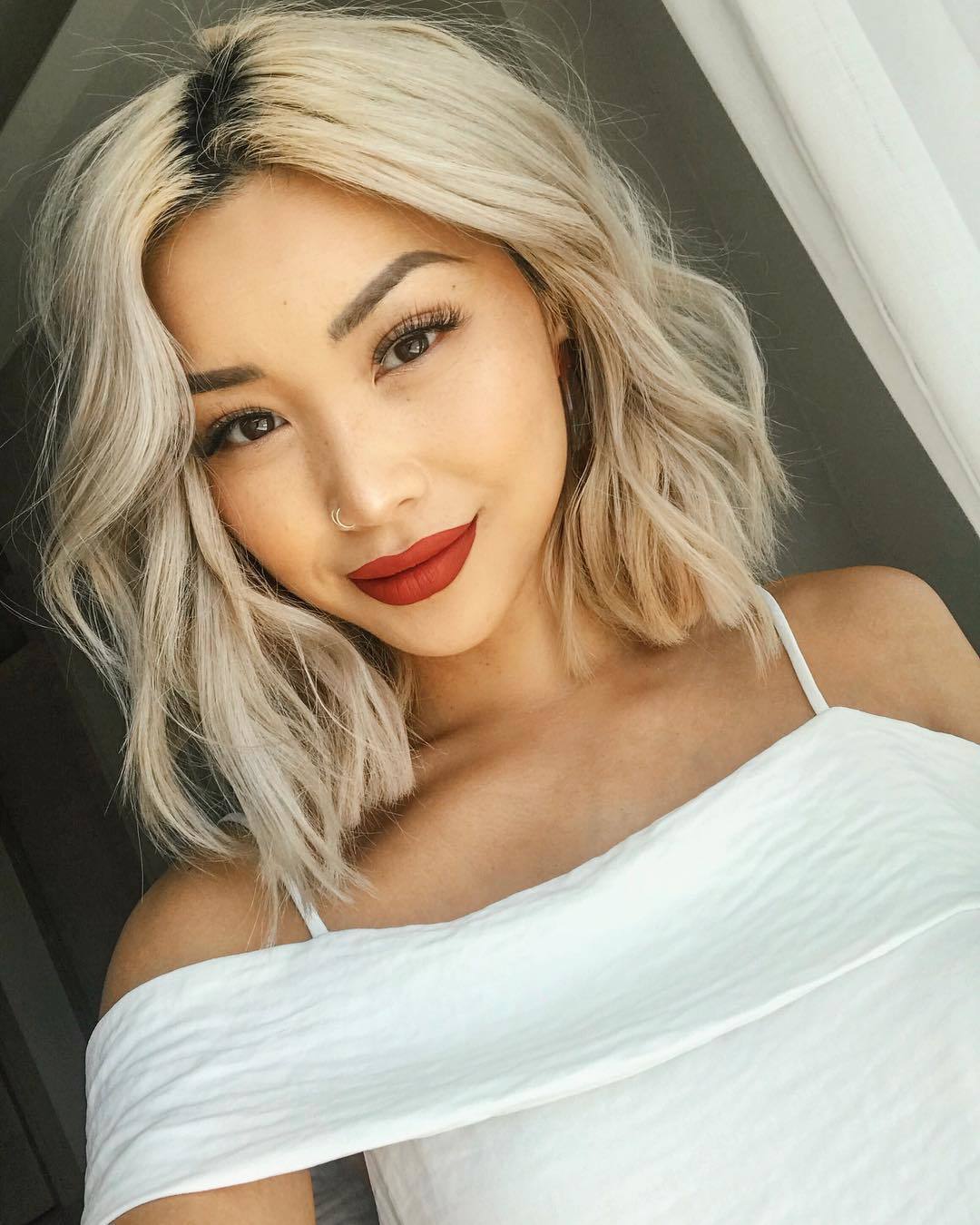 Femme asiatique avec une coupe de cheveux blonde, bouclée et longue.