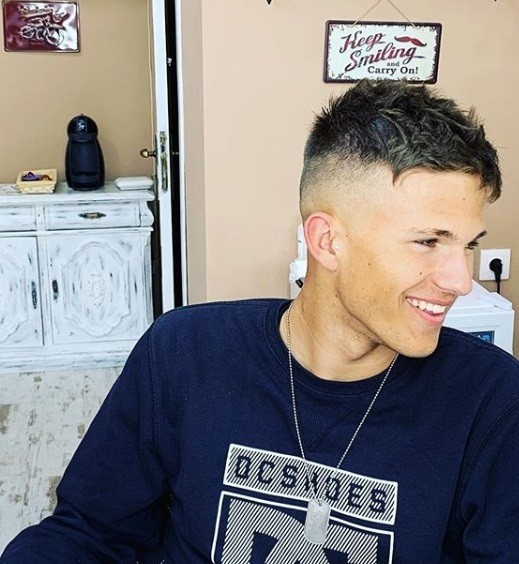 Qu'est-ce qu'une sous-coupe : Homme souriant aux cheveux bruns courts avec une texture désordonnée et une sous-coupe rasée.