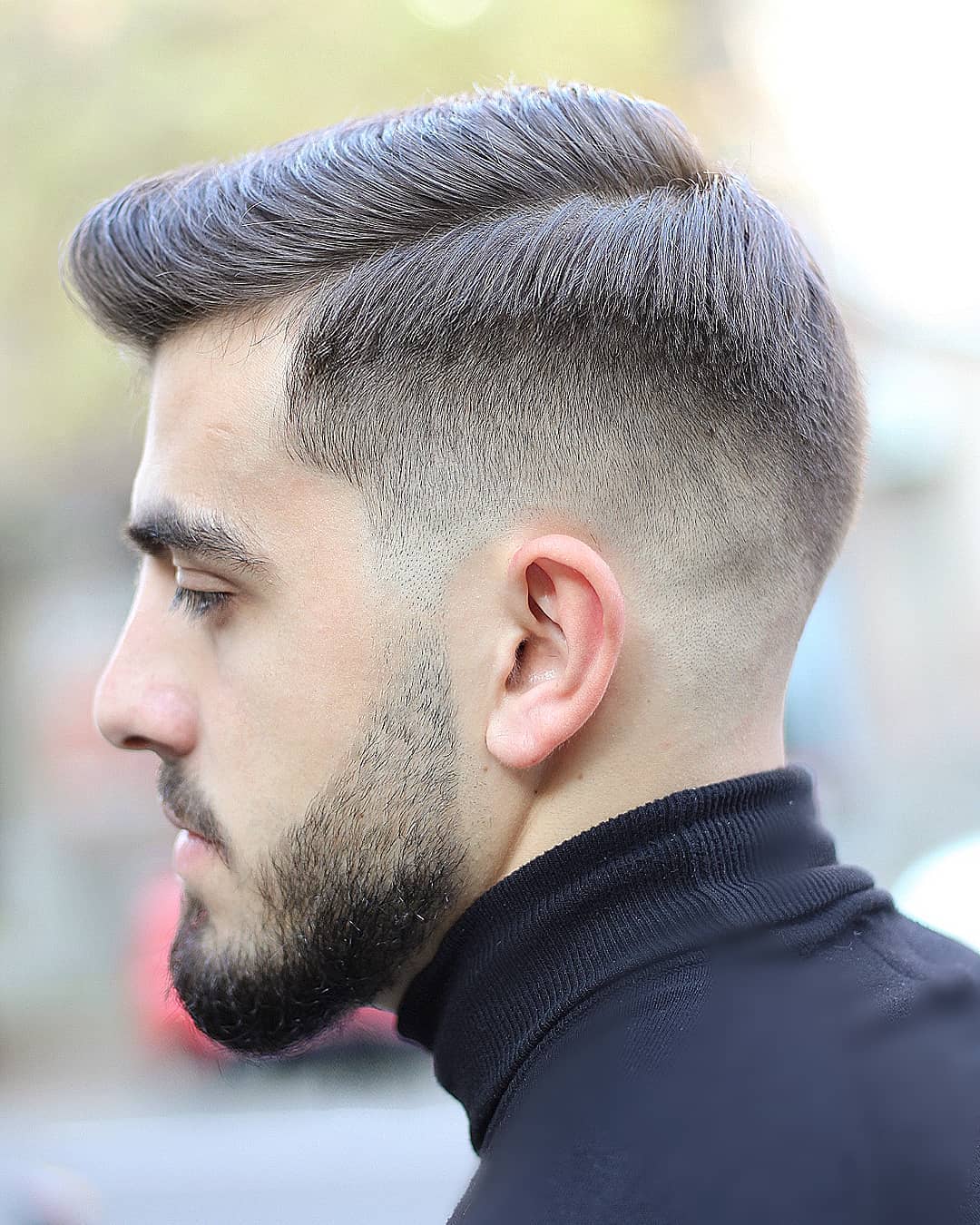 Homme aux cheveux bruns coiffés en peigne avec un dégradé bas.
