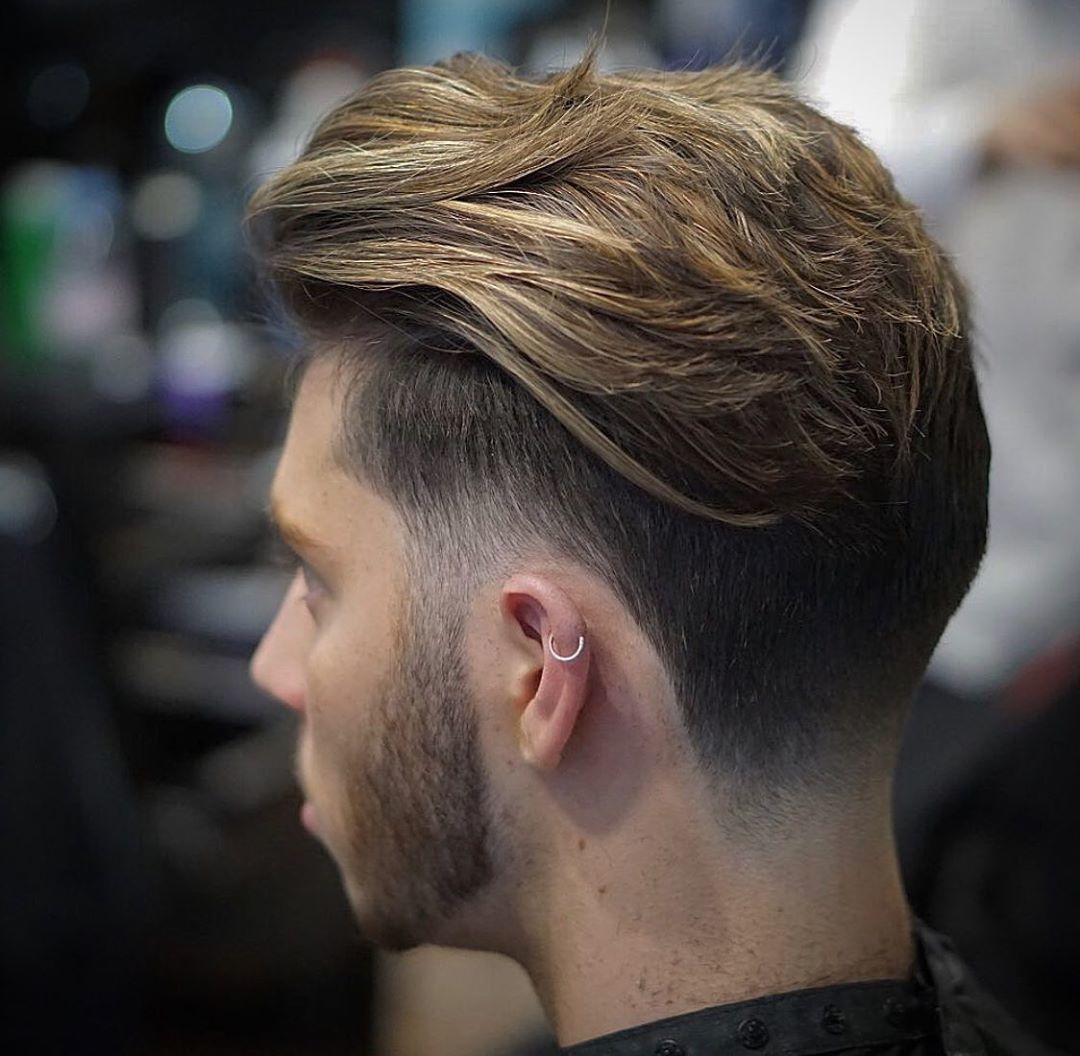 Homme aux cheveux bruns texturés de longueur moyenne avec une sous-coupe et une barbe.