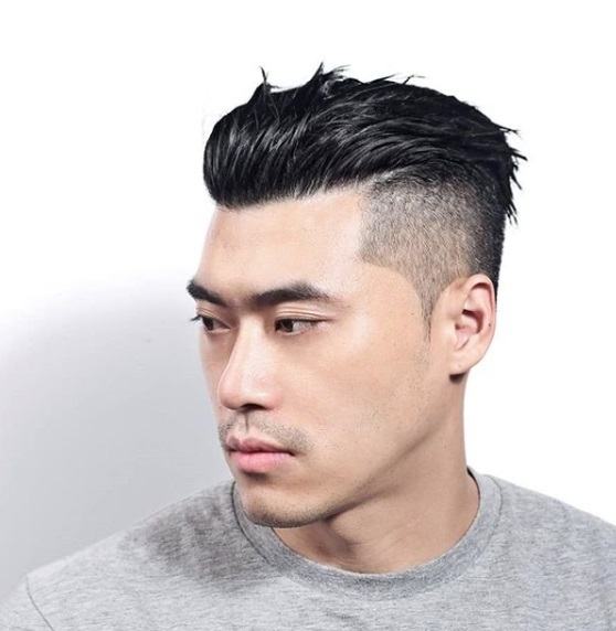 Homme aux cheveux bruns foncés gominés avec une sous-coupe, portant un t-shirt gris.