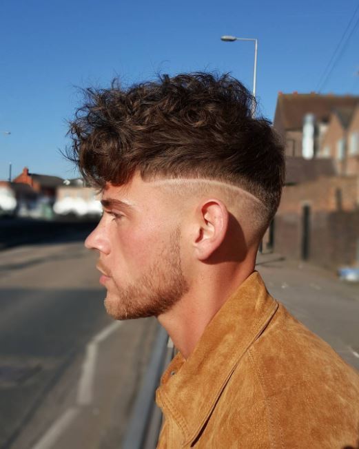 Vue de côté d'un modèle masculin aux cheveux bruns bouclés avec une coupe chirurgicale.