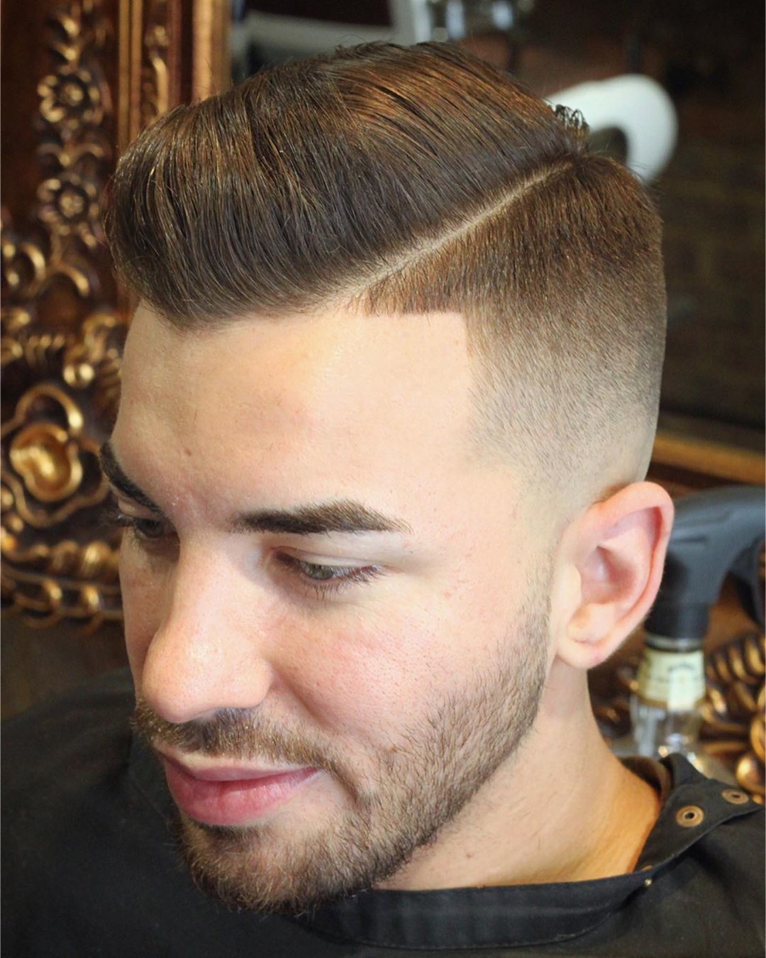 Homme aux cheveux bruns avec une coupe de cheveux avec une raie sur le côté et un dégradé.