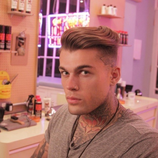un homme brun assis sur une chaise de coiffeur avec une coiffure en forme de quiff et une sous-coupe.