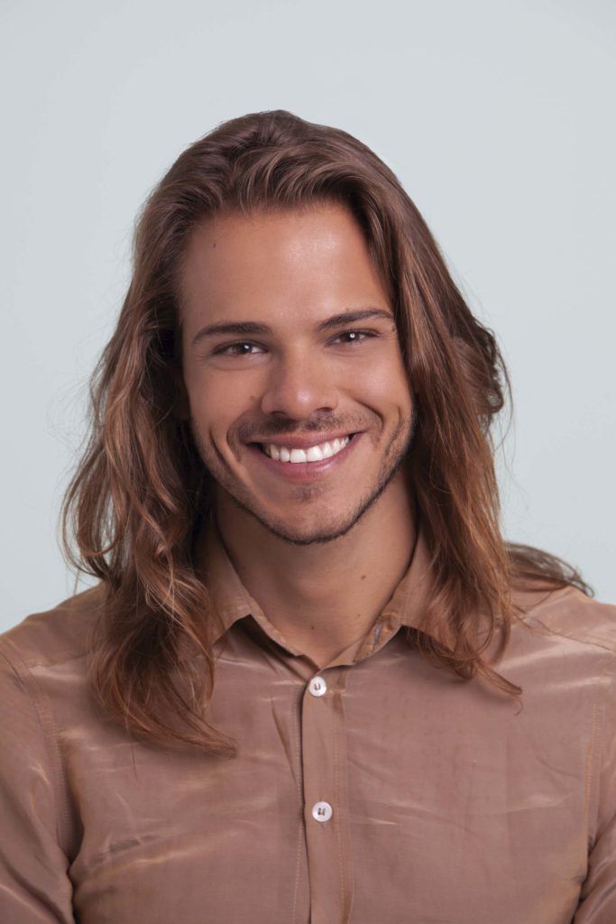 Un homme aux cheveux longs souriant à la caméra.