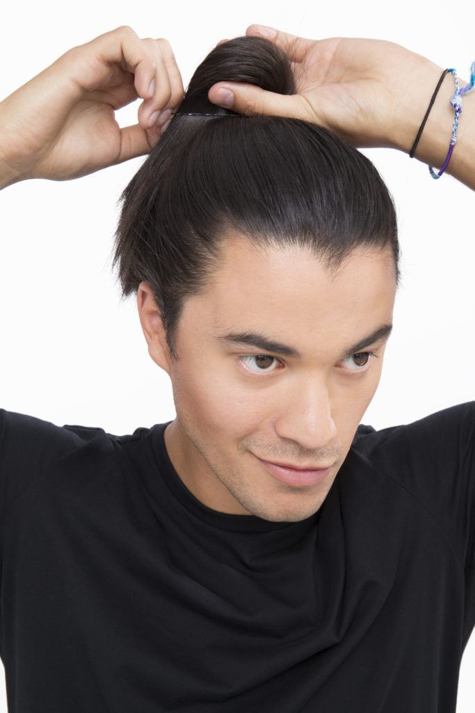 Homme aux cheveux noirs attachant ses cheveux bruns.