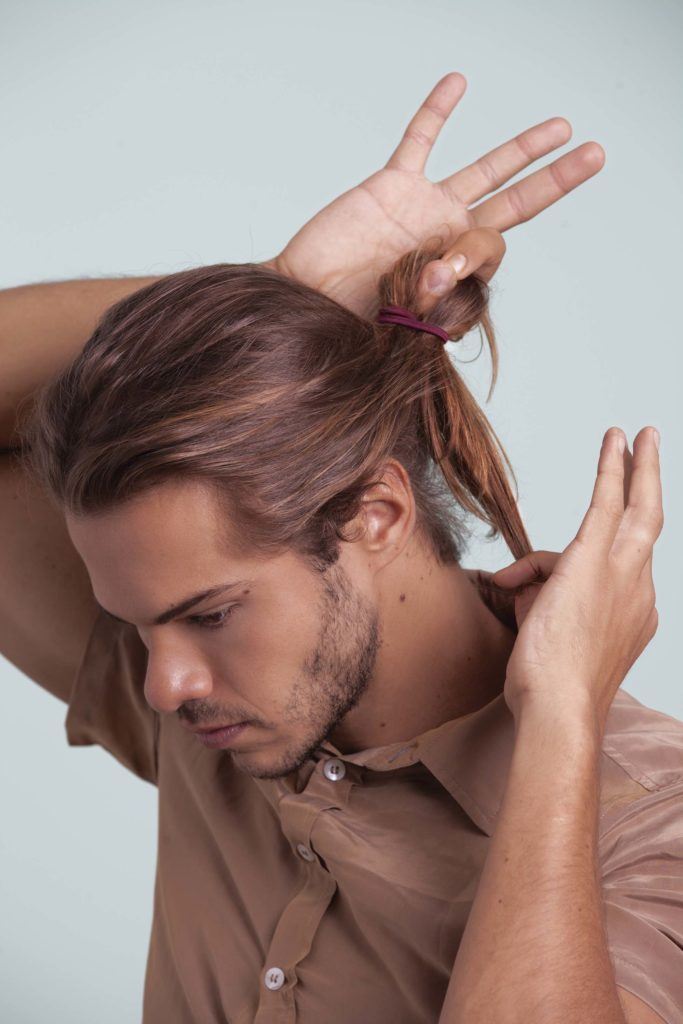 Tutoriel sur le chignon d'homme - homme regardant loin de la caméra et attachant ses cheveux.