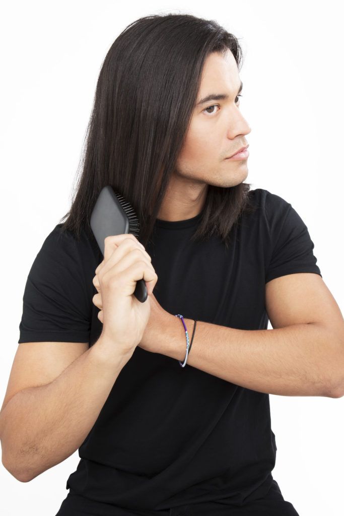 Homme aux cheveux bruns brossant ses cheveux bruns.