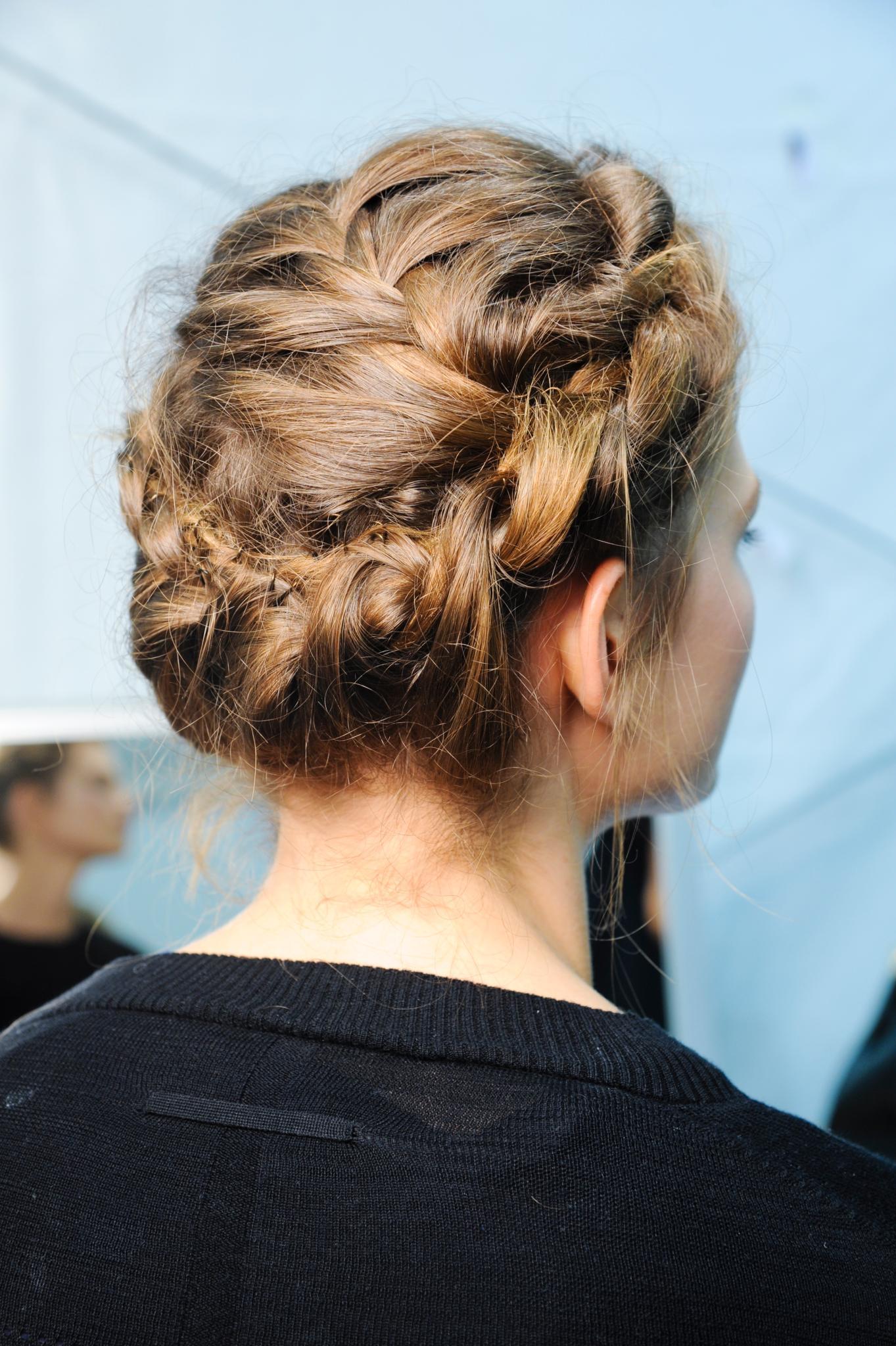 Plan de côté d'une femme avec des cheveux bruns moyens coiffés en couronne, portant un haut noir et posant dans les coulisses.