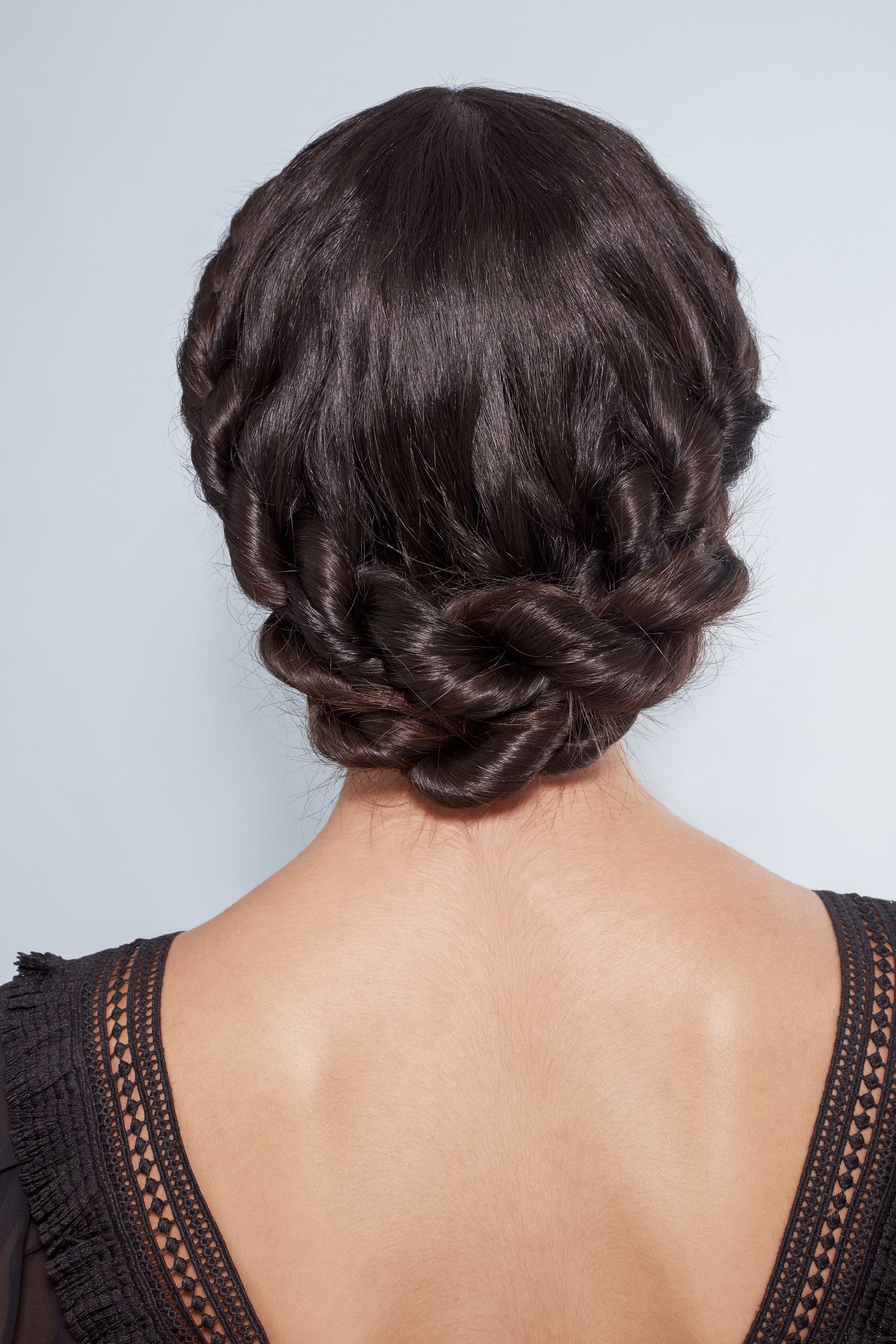 Plan arrière d'une femme aux cheveux bruns foncés coiffés en une tresse couronne torsadée, vêtue de noir et posant dans le studio Poudre de Rose UK.