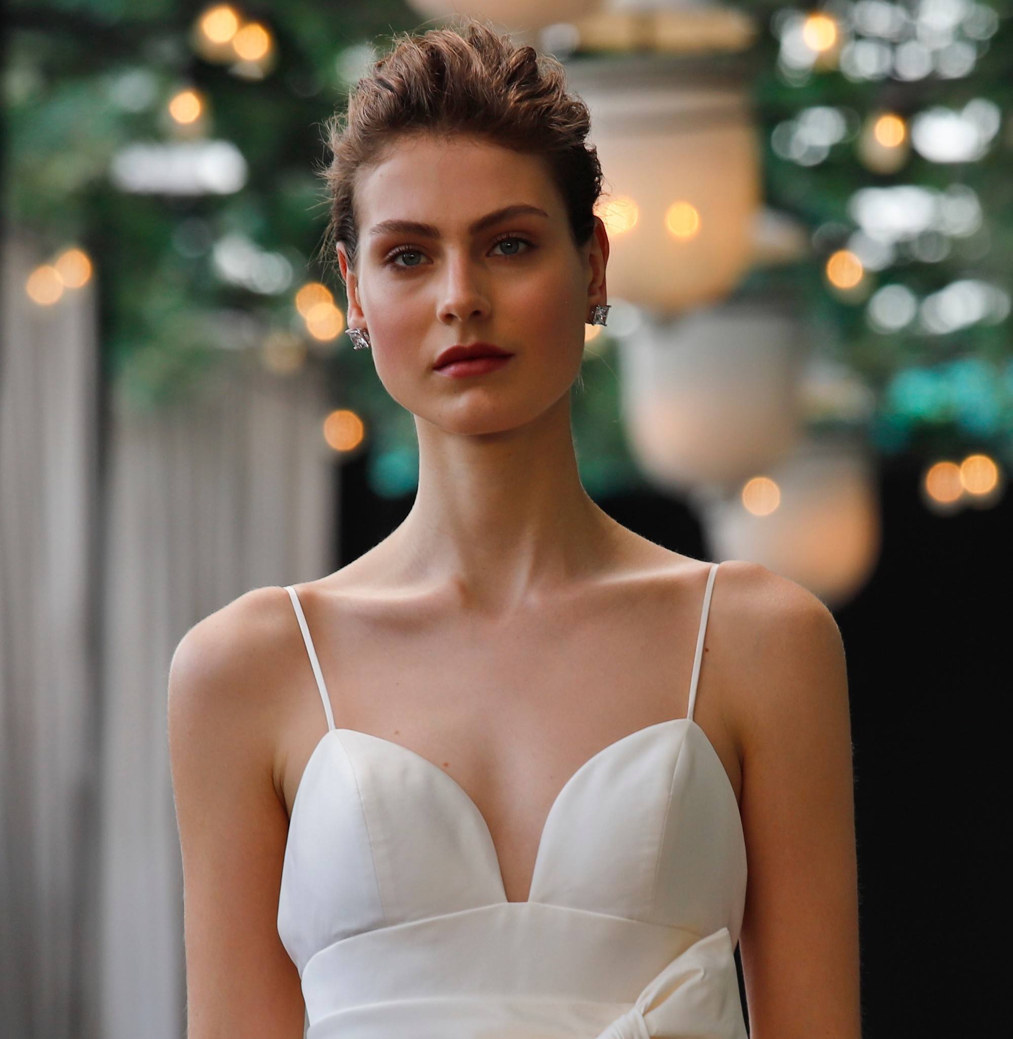 Prise de vue d'un mannequin sur un podium de mariage avec des cheveux courts coiffés en un quiff ébouriffé, balayé vers l'arrière, habillé tout en blanc.