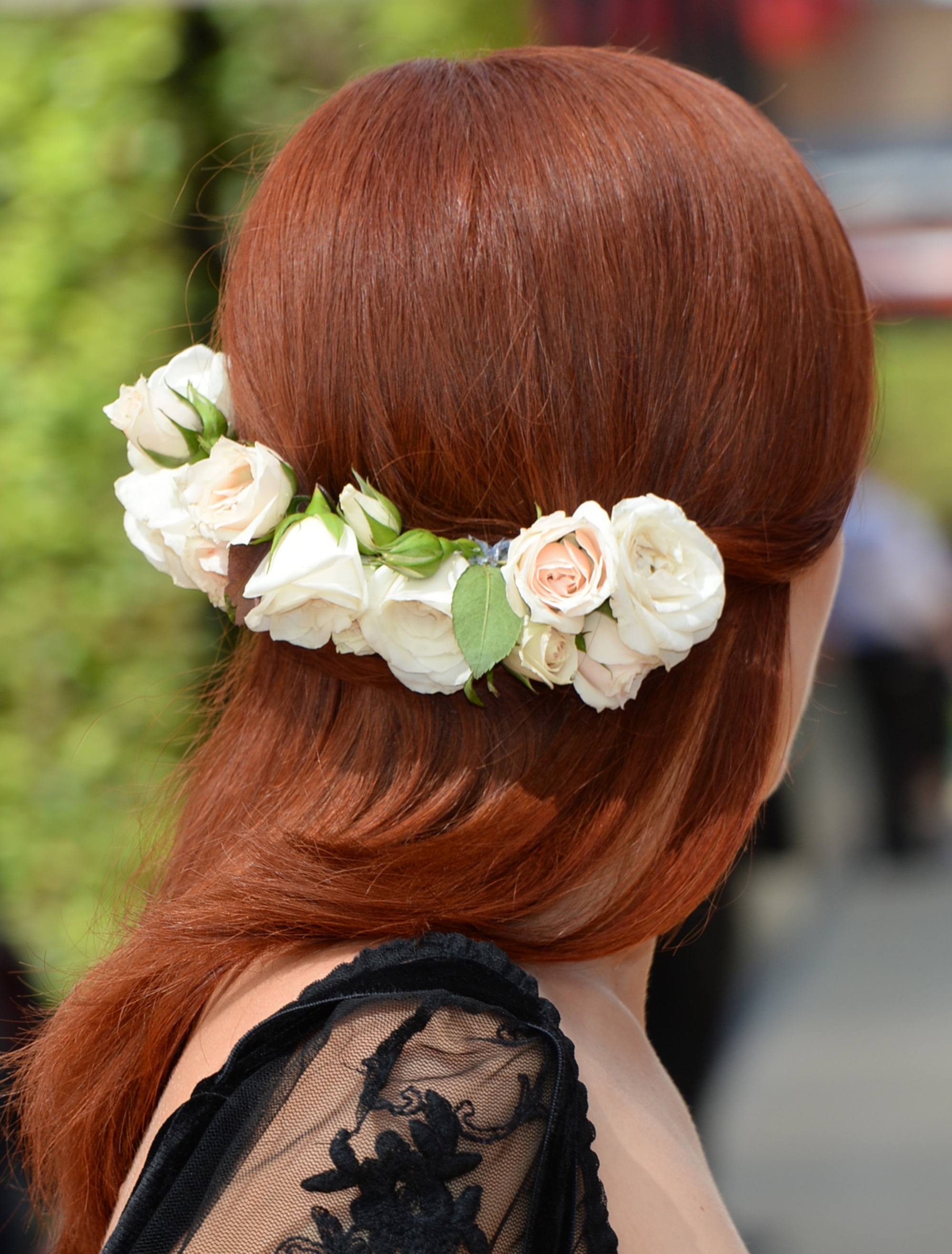 Coiffure d'une invitée de mariage : Plan arrière d'une femme aux cheveux roux cuivrés coiffés à la perfection, portant une épingle à cheveux basse à fleurs avec un haut en filet noir.