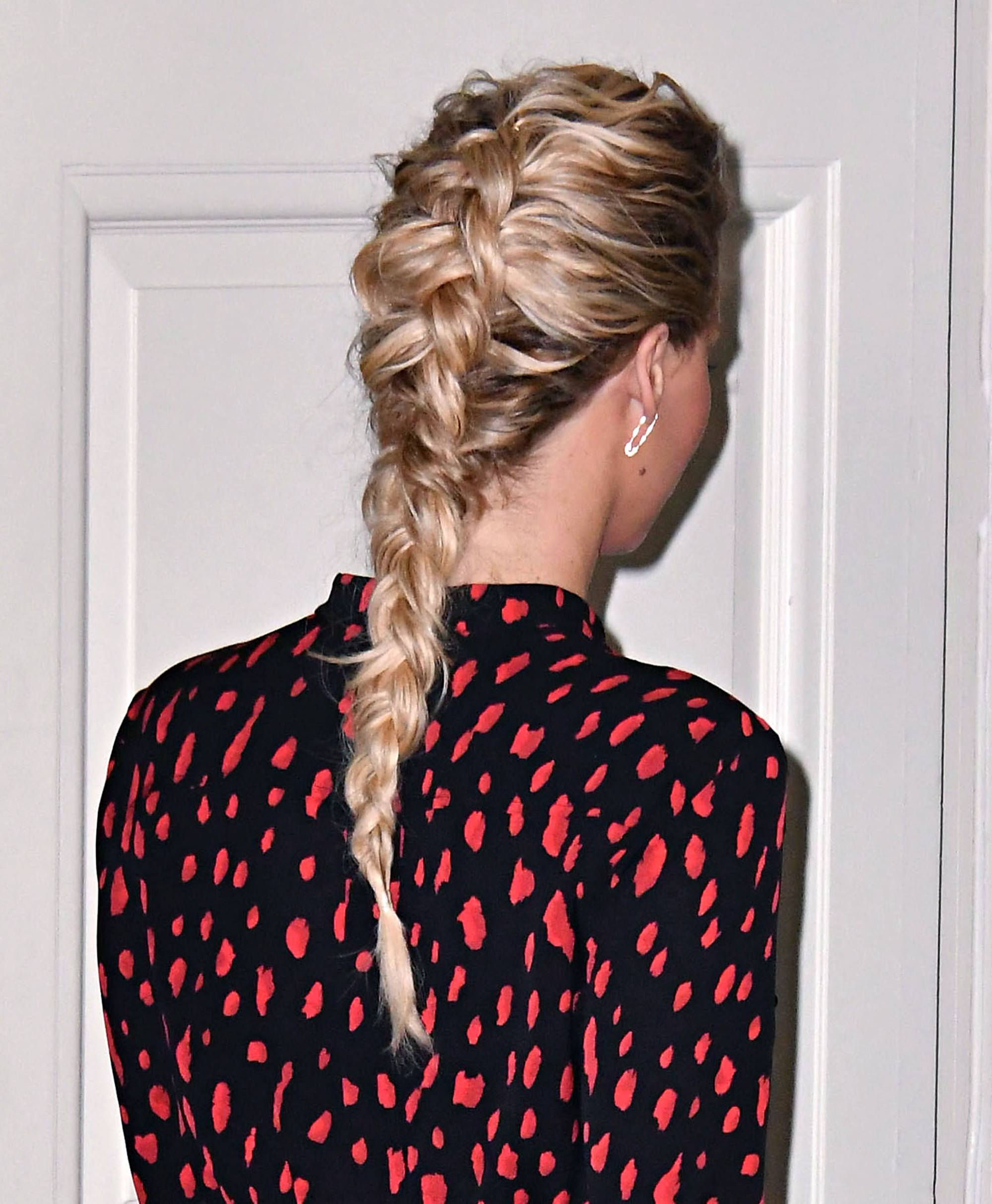 Plan arrière d'une femme aux cheveux blonds dorés coiffés en tresse française inversée, portant une robe tachetée.
