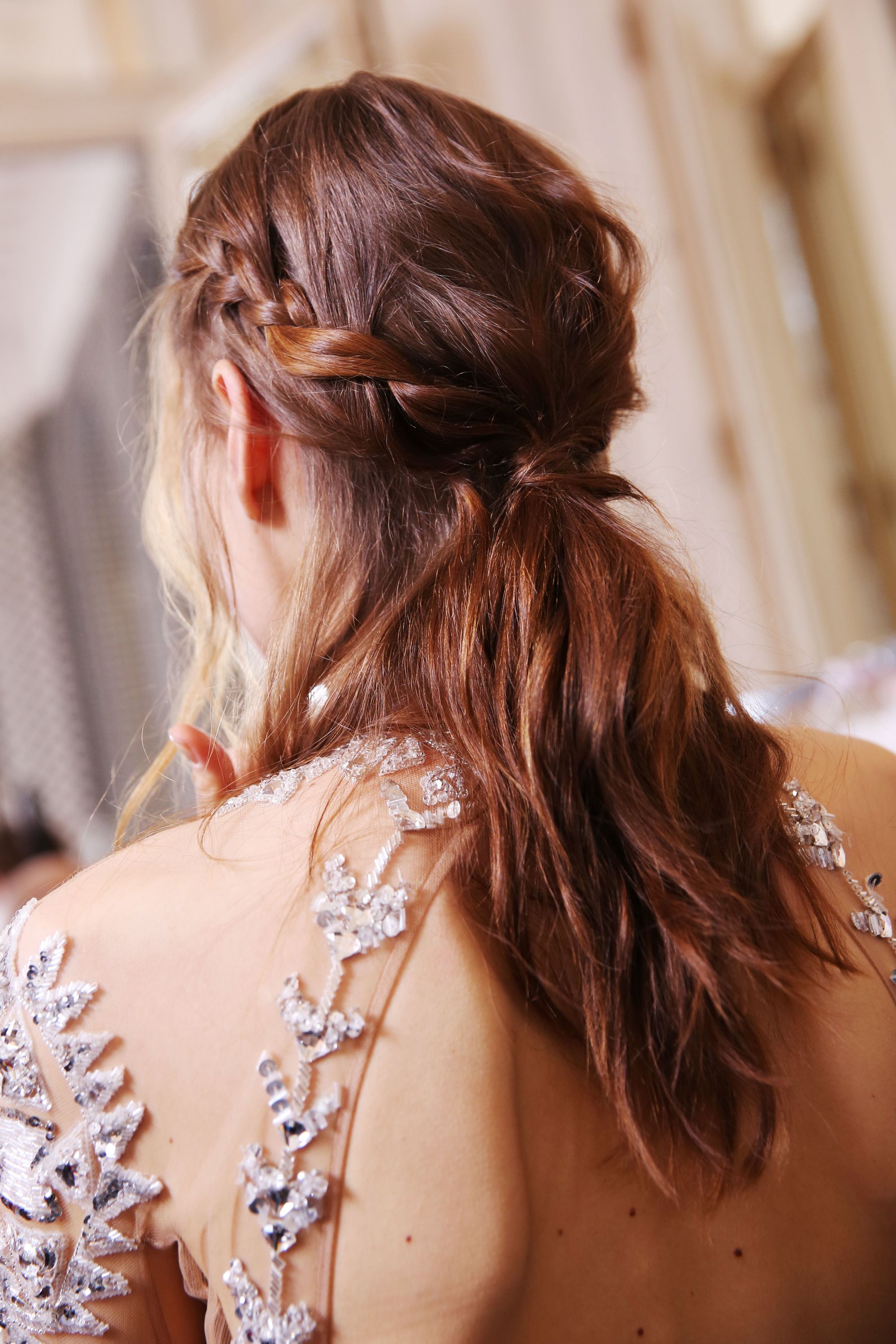 mannequin brune en coulisses portant une robe brodée transparente avec des cheveux tressés, mi-hauts mi-bas.