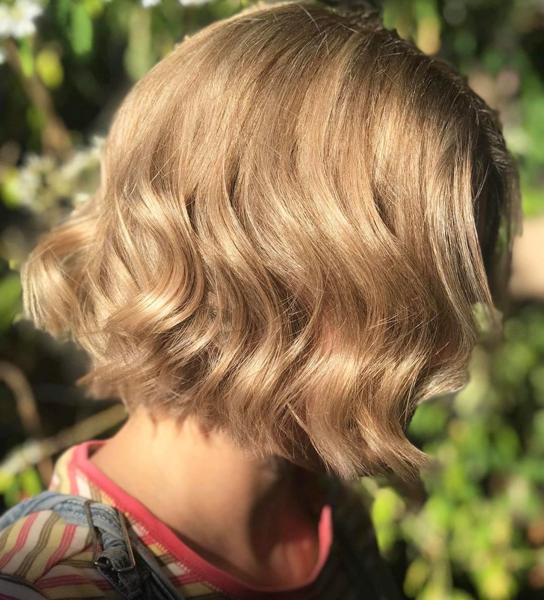 Femme avec une coupe courte ondulée blonde miel clair.