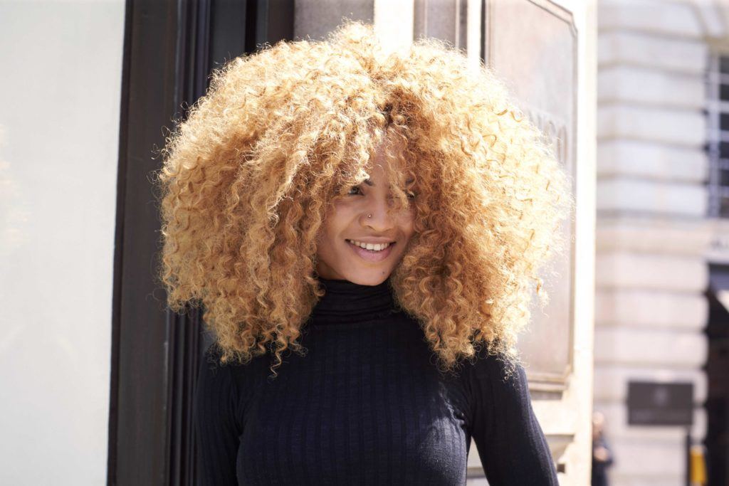 vue de face d'une femme aux grands cheveux bouclés dans une nuance de couleur blonde miel cuivré 