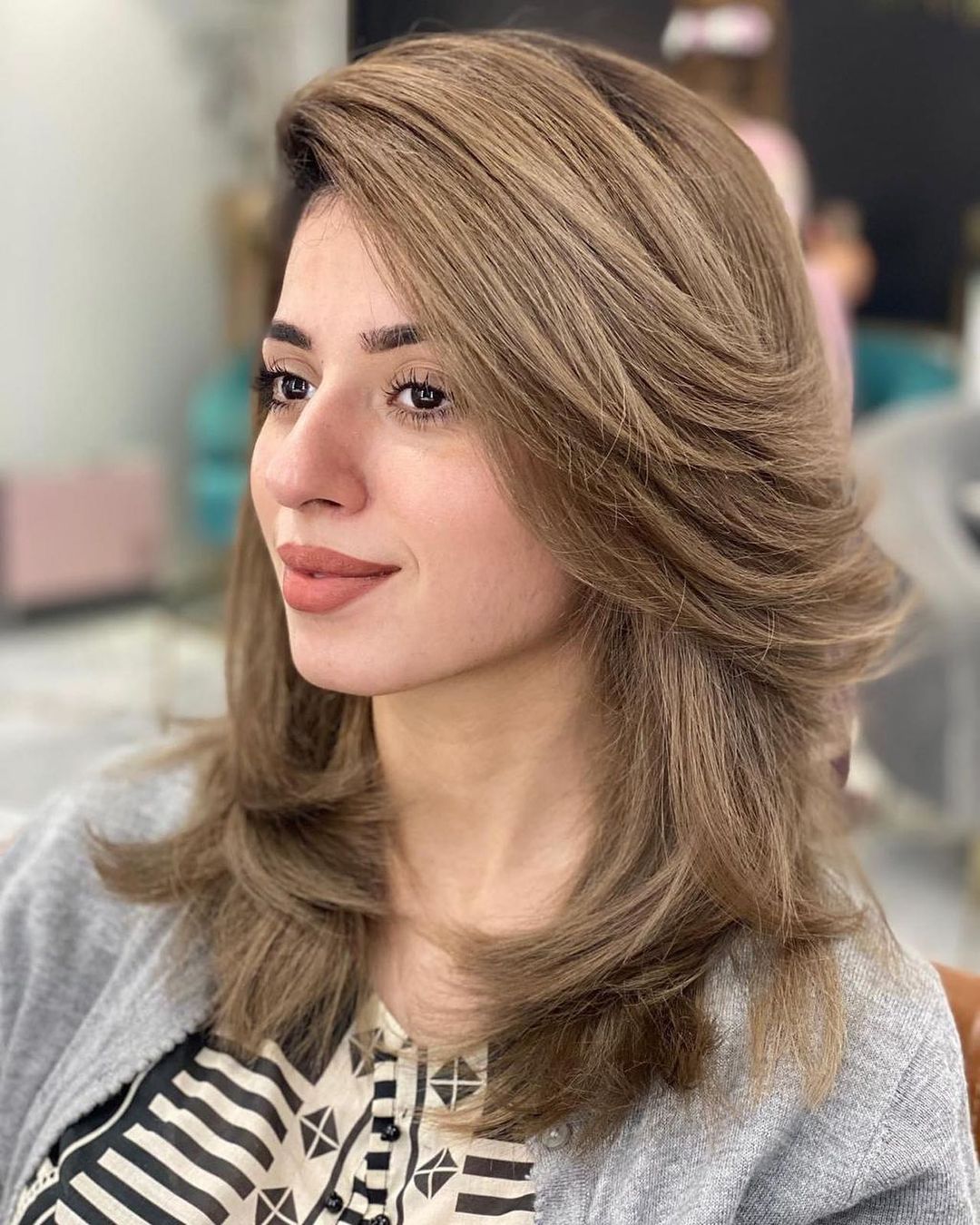 Coupe de cheveux moderne de longueur moyenne avec des couches de plumes dans un style balayé sur le côté