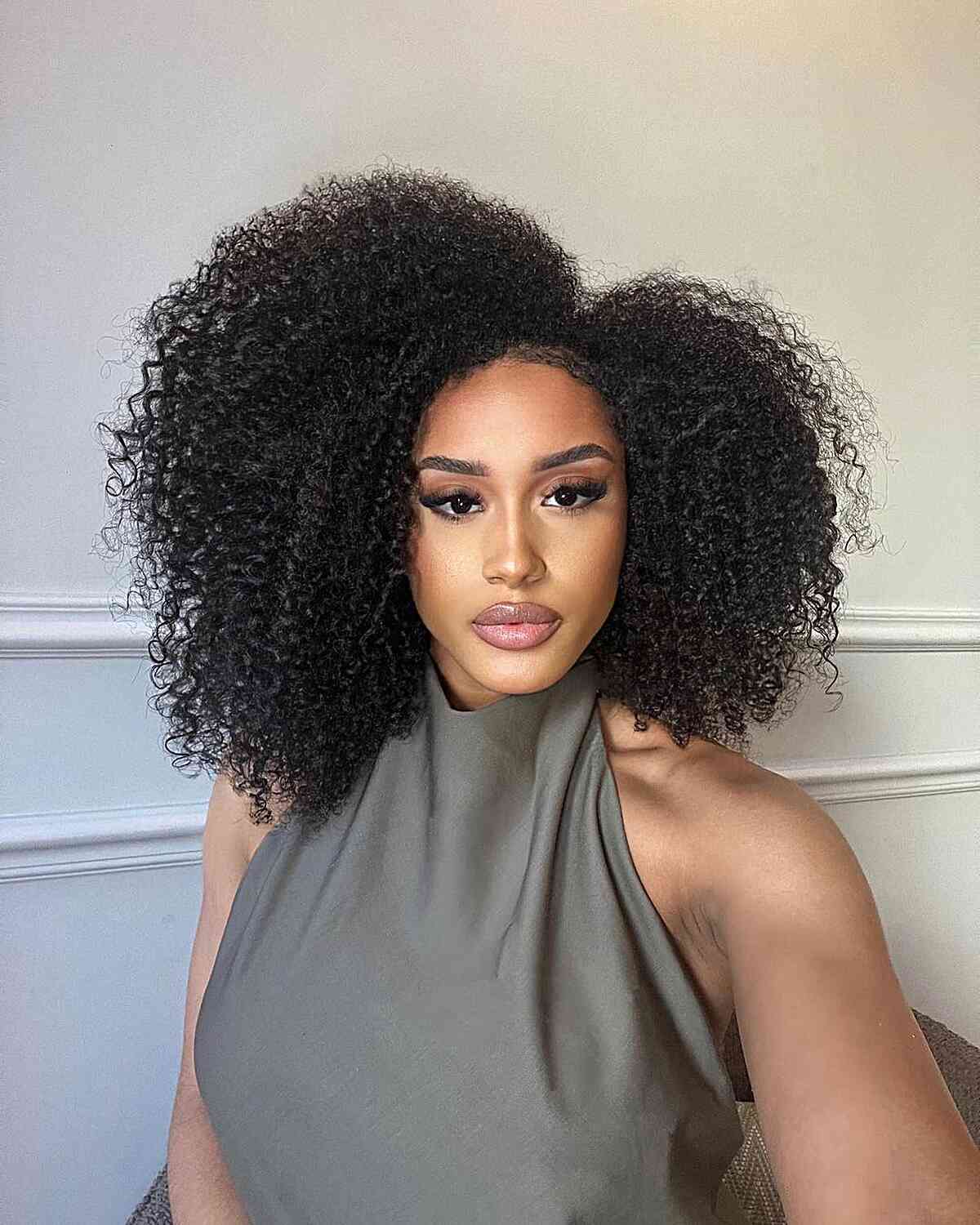 Une femme avec une coupe Cadō afro moyenne avec une raie sur le côté, embrassant le volume et la texture naturels de la chevelure avec une touche asymétrique.