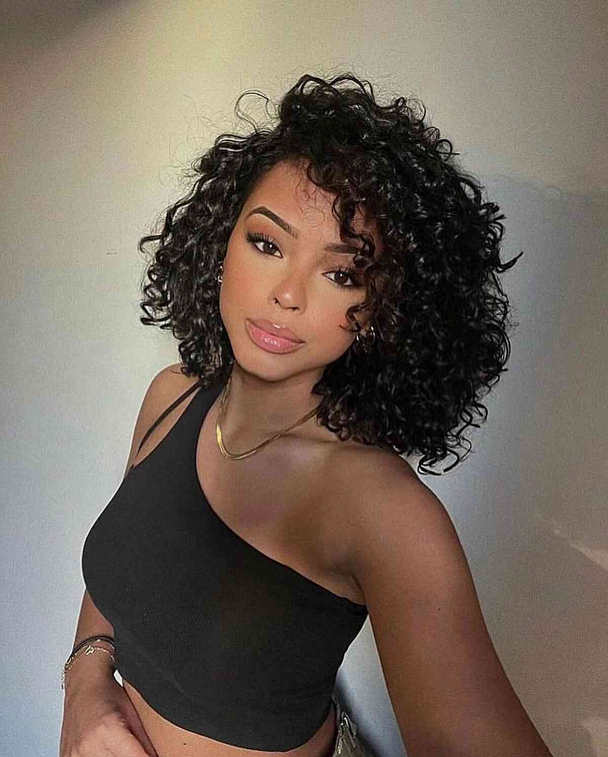 Une femme avec une coupe Cadō comprenant des cheveux courts et bouclés et une raie latérale profonde, offrant un style dramatique et volumineux.