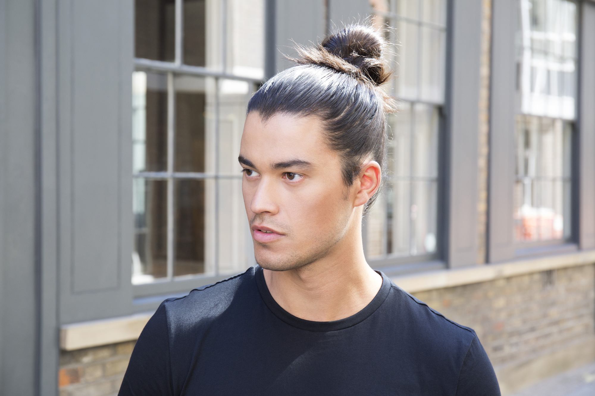 Tutoriel sur le chignon d'homme : homme brun regardant loin de la caméra, debout dans la rue.