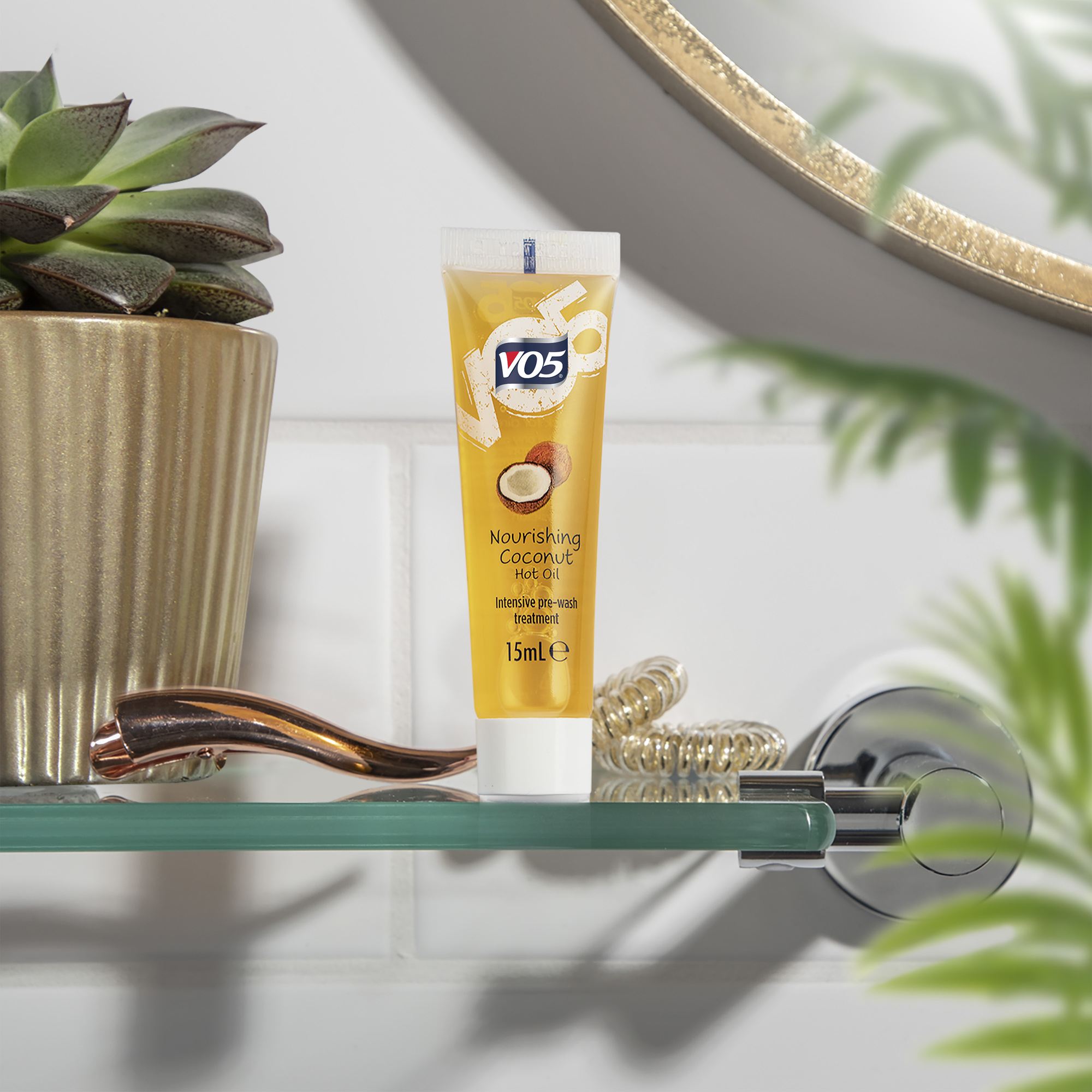 Les traitements à l'huile chaude : Prise de vue de l'huile de noix de coco nourrissante VO5 dans une salle de bain, avec des plantes contre un mur blanc.